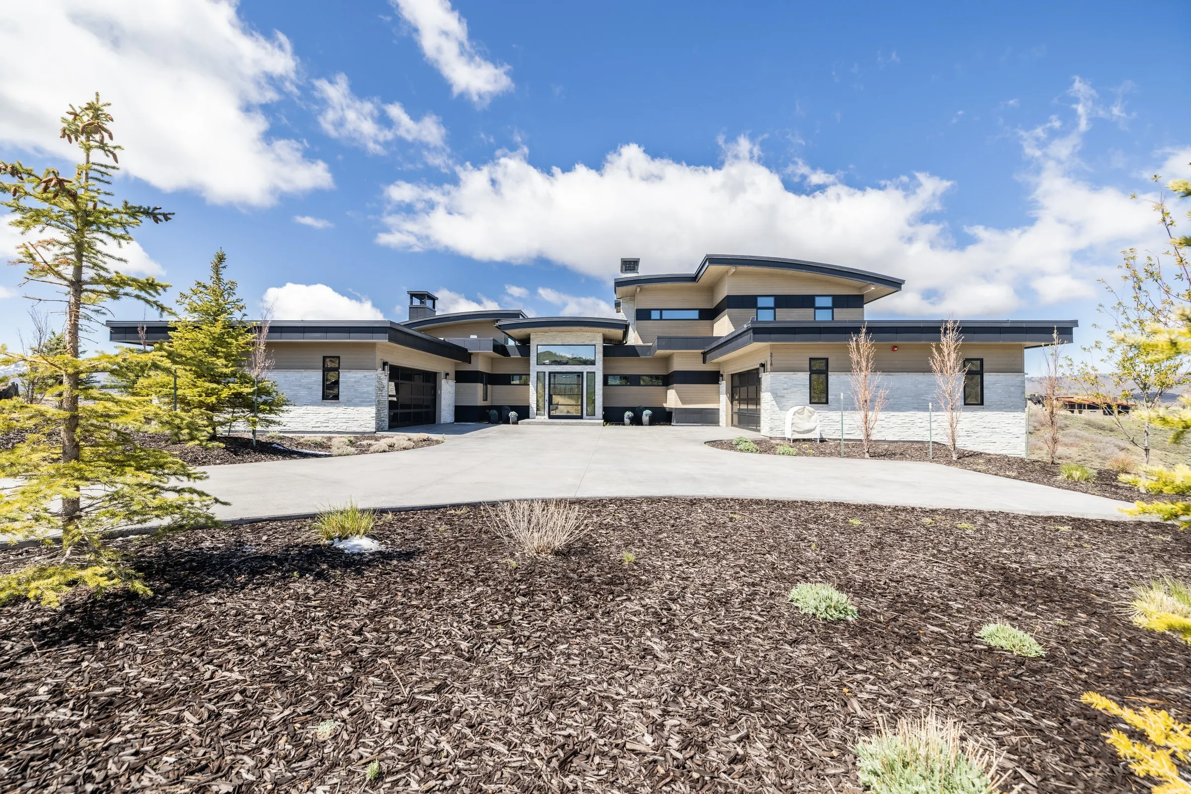 Custom home in Park City, Utah with a curved standing seam roof, stone and wood siding, and a wide circular driveway
