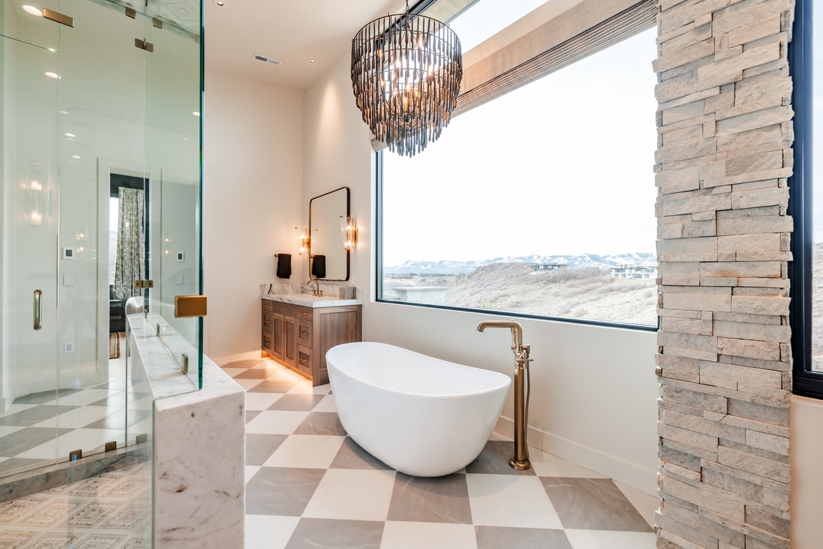 Pinnacle Lot 47 Park City Utah — oval soaking tub beneath cascading chandelier with stacked-stone accent wall and valley views