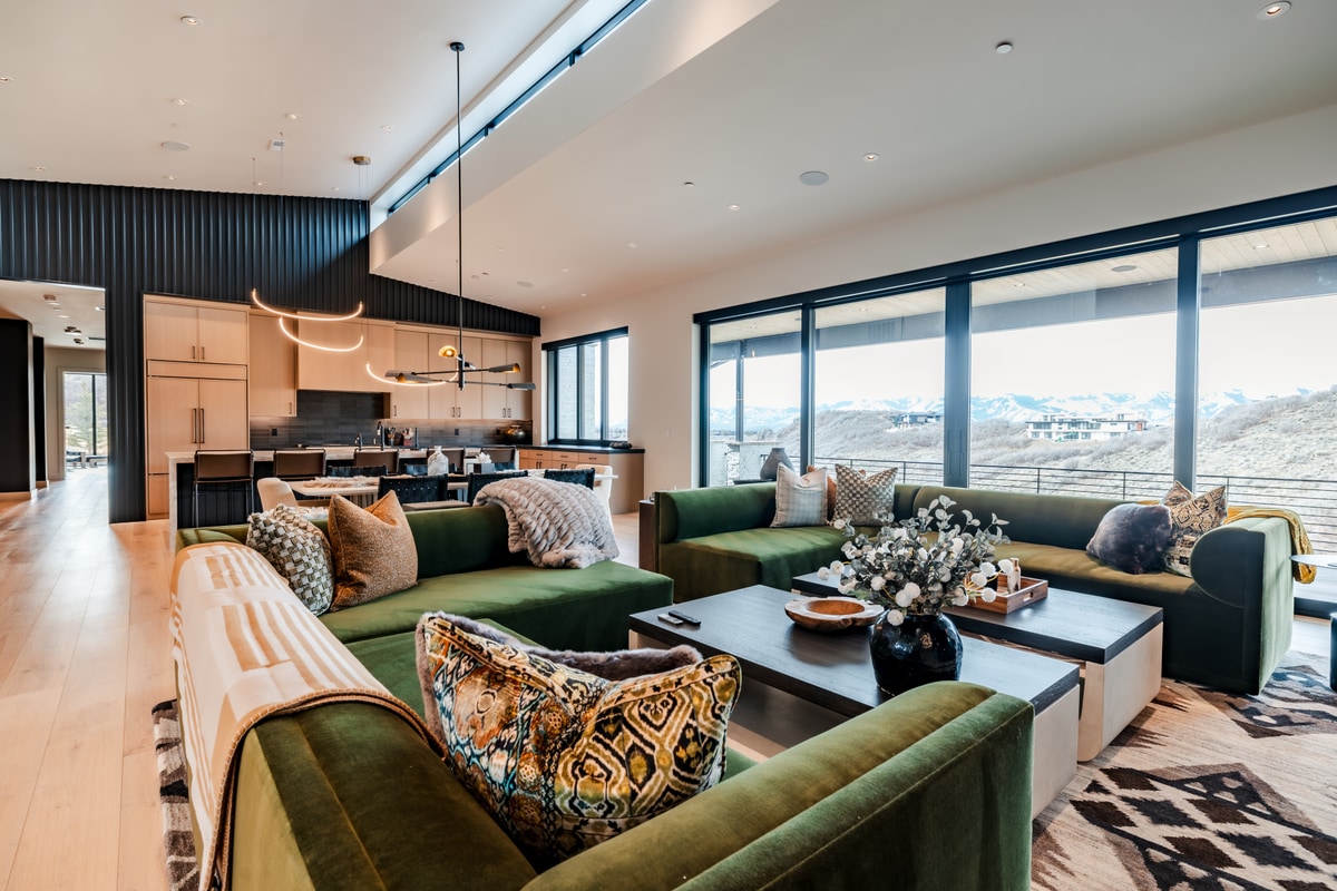 Pinnacle Lot 47 Park City Utah — great room toward kitchen with green velvet seating, snow-mountain views, and sculptural pendant
