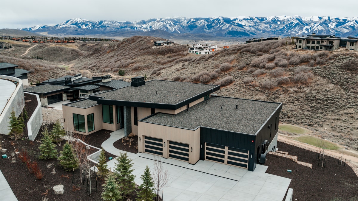 Pinnacle Lot 49 Park City Utah — aerial front facade with three-car garage, flat roofline, and sweeping Wasatch Range backdrop