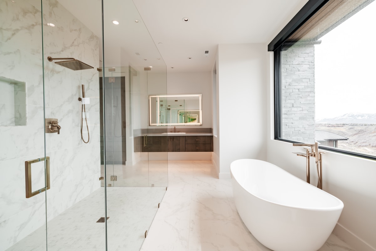 Pinnacle Lot 49 Park City Utah — primary bath with marble slab shower walls, brushed gold rain-head fixtures, and freestanding tub