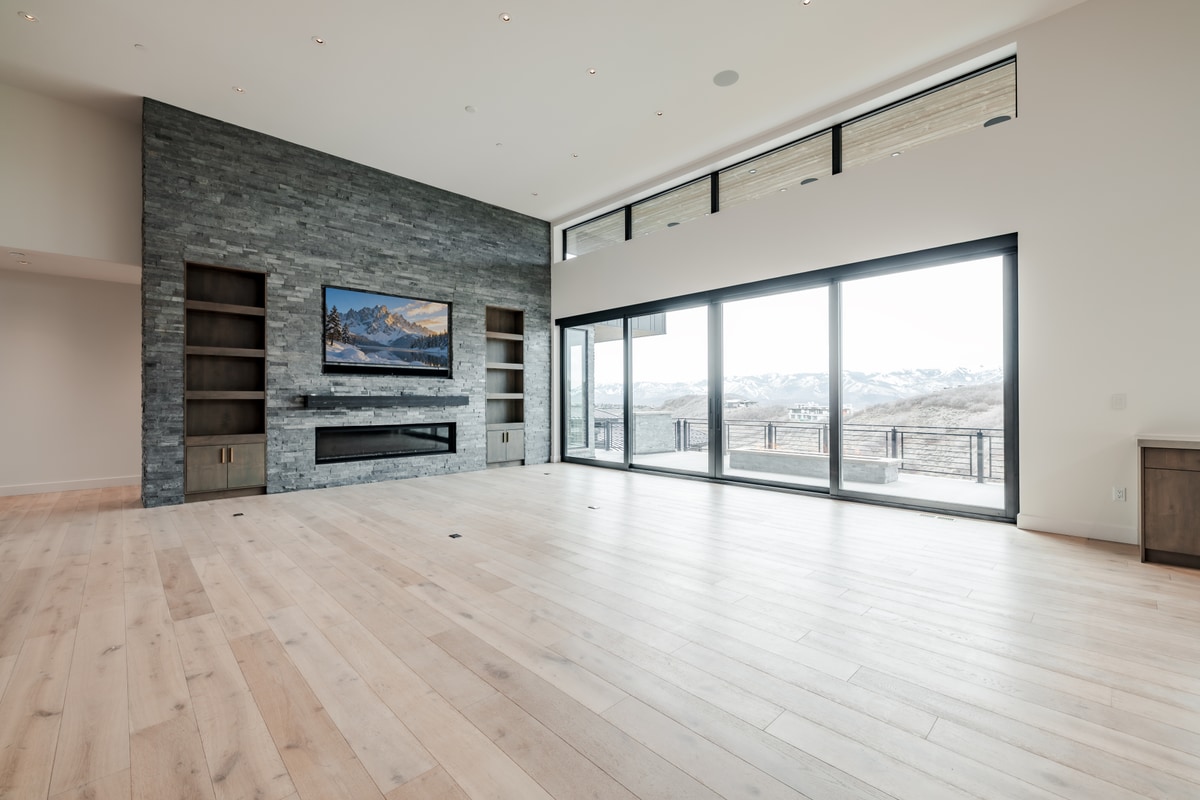 Pinnacle Lot 49 Park City Utah — great room with stacked ledger stone fireplace, built-in shelving, and wall of sliding glass doors