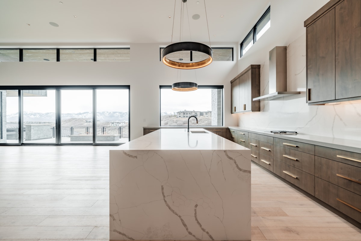Pinnacle Lot 49 Park City Utah — kitchen island in book-matched quartz with waterfall edge beneath drum pendant lights