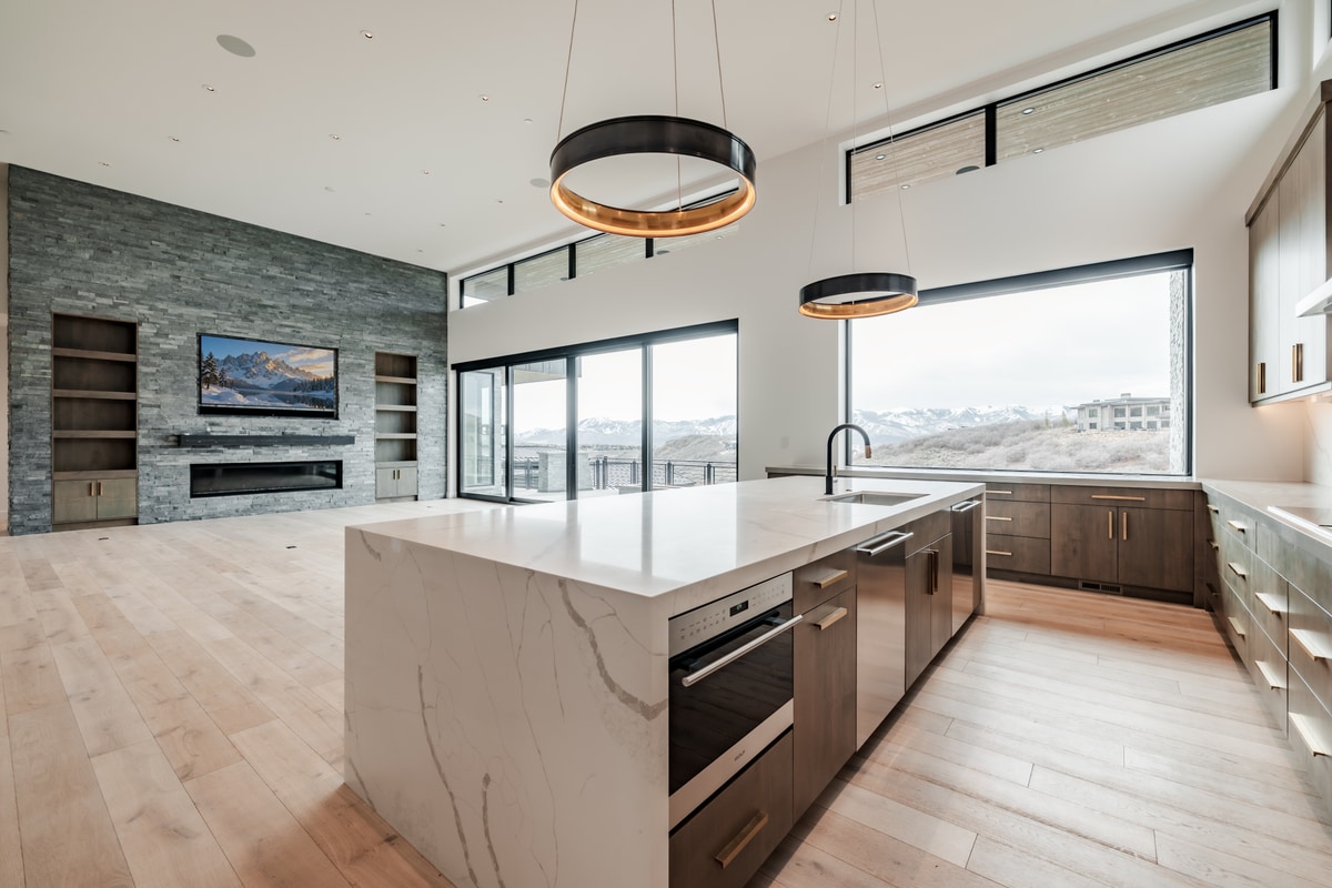 Pinnacle Lot 49 Park City Utah — open-plan kitchen and great room with quartz island, stone fireplace, and panoramic glass walls