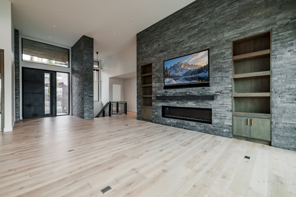 Pinnacle Lot 49 Park City Utah — double-height entry hall with ledger stone column, steel-rail staircase, and pivot door entry