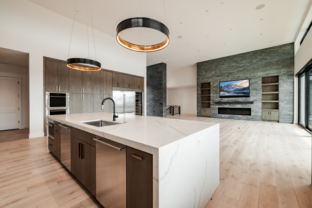 Pinnacle Lot 49 Park City Utah — kitchen-to-living vista with quartz island, stone fireplace wall, and sliding glass doors