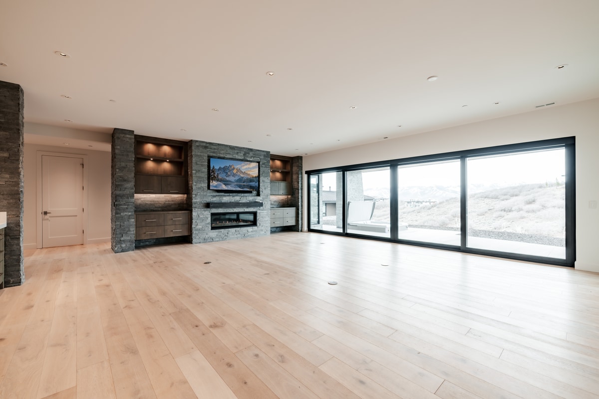 Pinnacle Lot 49 Park City Utah — lower-level family room with stone fireplace, built-in media niches, and sliding doors to hillside