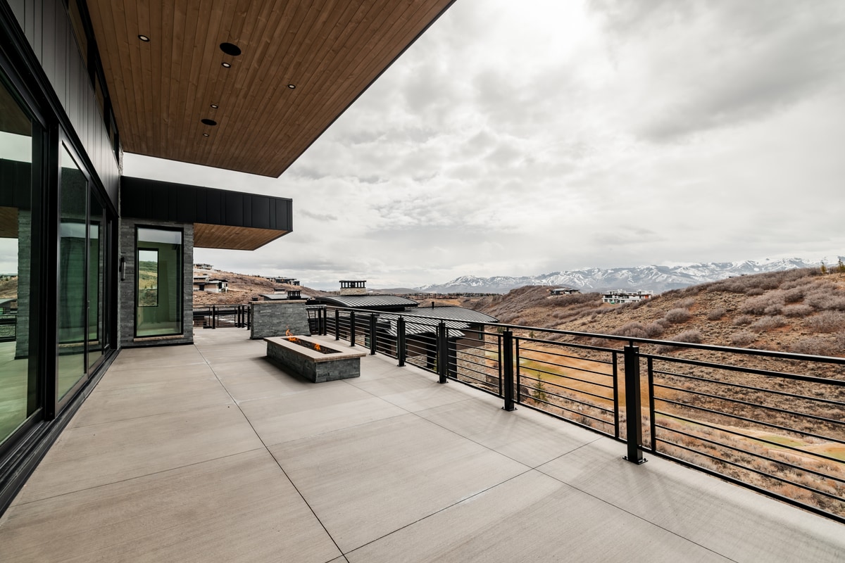 Pinnacle Lot 49 Park City Utah — covered upper deck with stone fire pit, steel railing, wood soffit, and Wasatch Range views