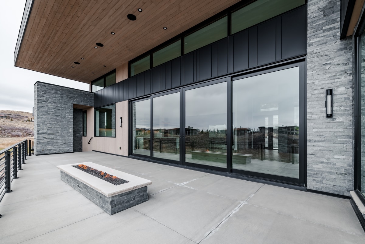 Pinnacle Lot 49 Park City Utah — outdoor terrace with recessed fire feature, stacked stone walls, and sliding glass doors