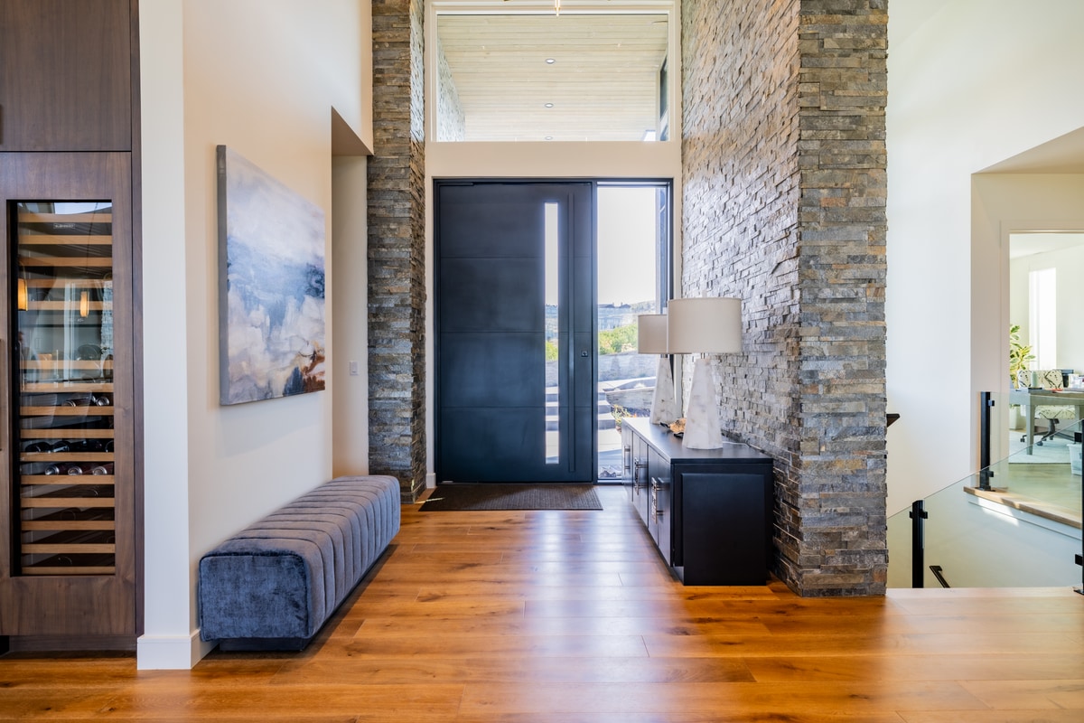 Promontory Lot 52 Park City Utah — grand entry foyer with double-height stacked-stone columns, pivot front door, and wine storage