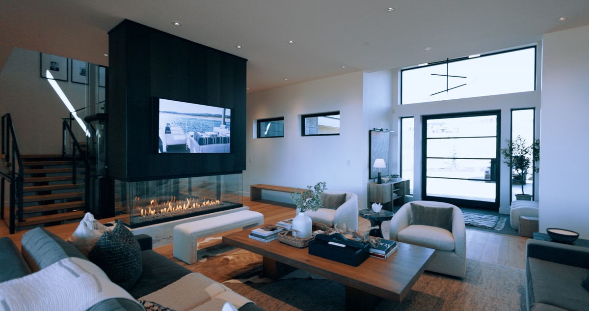 Promontory Model Home Park City Utah — double-height living room with see-through linear fireplace, black feature wall, glass staircase railing, and mountain panorama