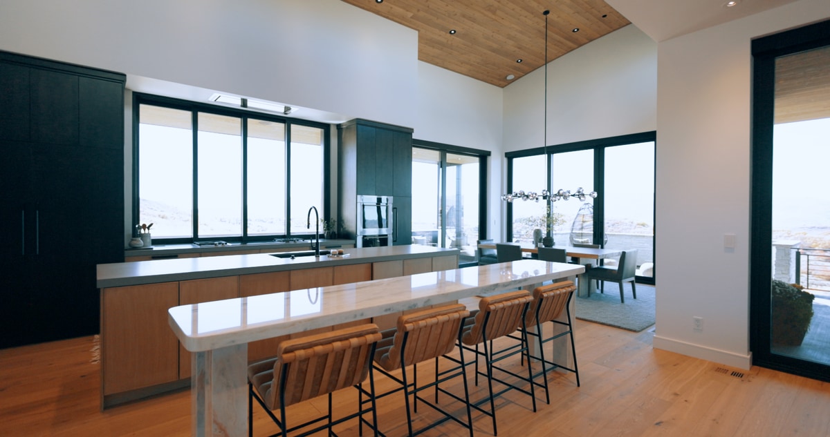 Promontory Model Home Park City Utah — gourmet kitchen with waterfall quartz island, leather barstools, wood ceiling inlay, and mountain-view dining nook