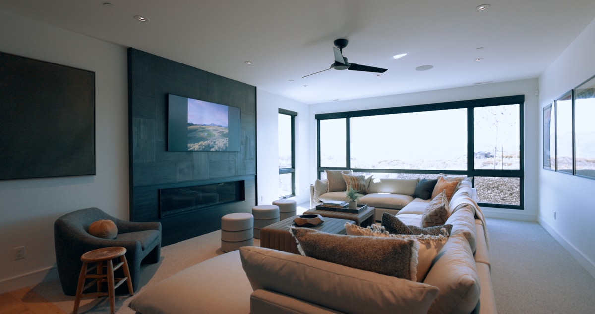 Promontory Model Home Park City Utah — secondary living room with dark panel fireplace wall, sectional sofa, and corner windows with mountain views