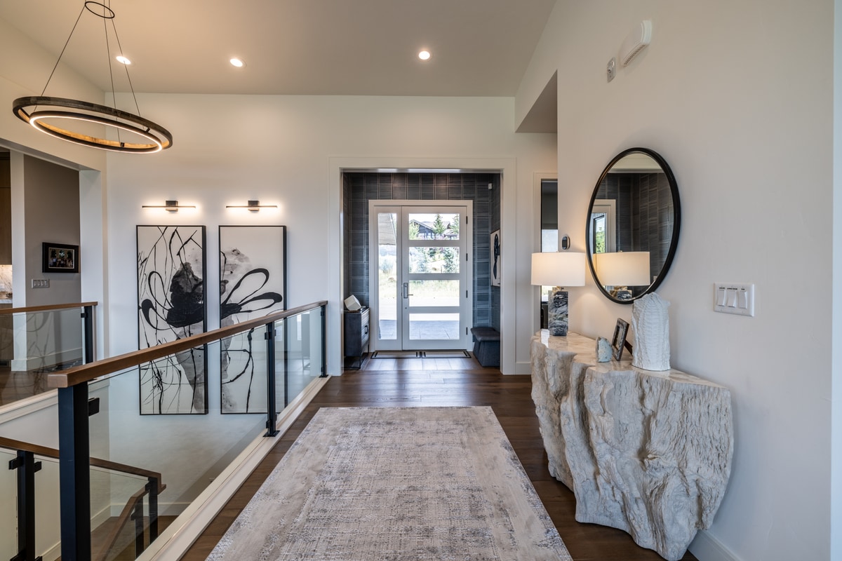 Ranch Gardens Park City Utah — entry foyer with raw stone console table, circular pendant, glass-railed landing, and pivot front door