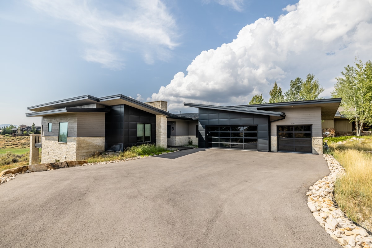 Ranch Gardens Park City Utah — street-level front elevation with board-formed stone base, dark metal cladding, and glass garage doors