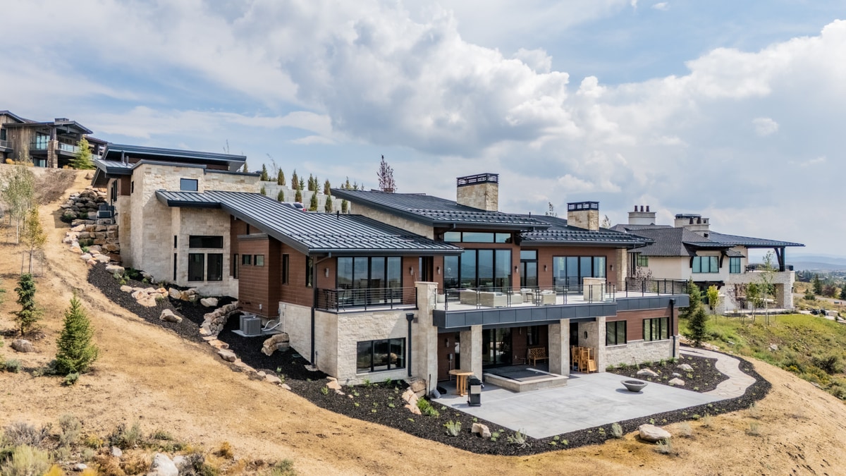 Summit Estates Park City Utah — exterior rear elevation with standing seam metal roof, stone cladding, and covered deck overlooking hillside