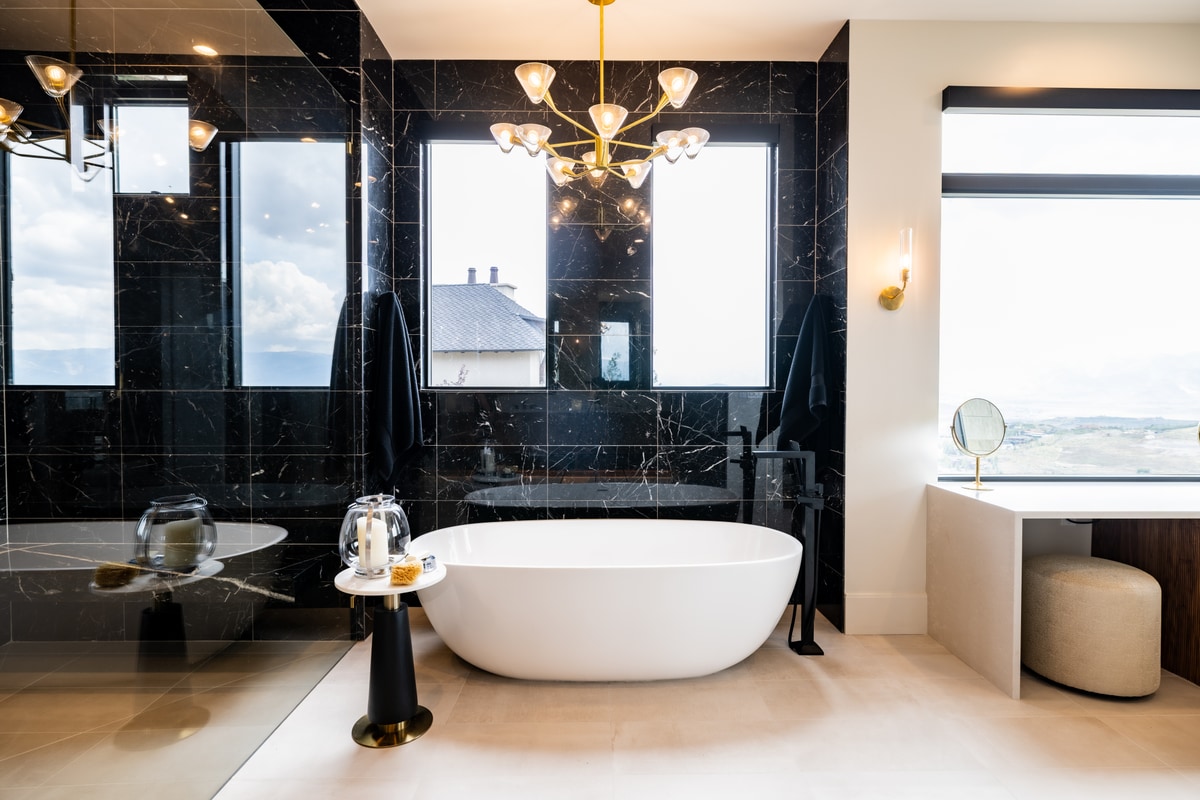 Summit Estates Park City Utah — primary bathroom with black marble tile, freestanding soaking tub, brass chandelier, and mountain views