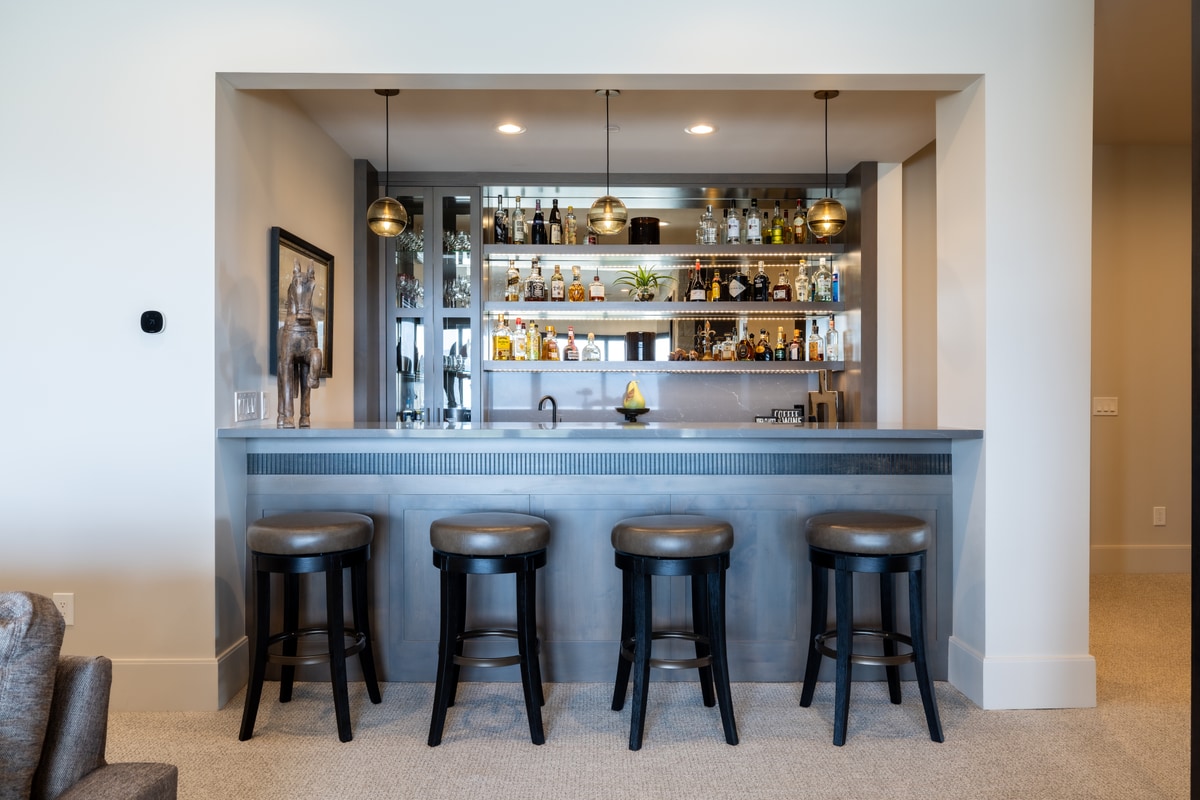 Summit Estates Park City Utah — lower-level wet bar with fluted concrete countertop, mirrored backlit shelves, and globe pendants