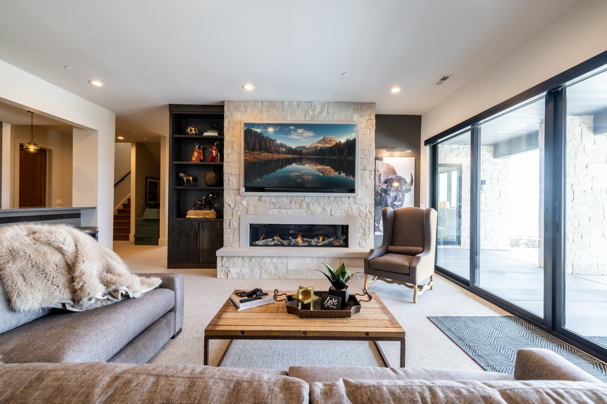 Summit Estates Park City Utah — lower-level family room with travertine fireplace surround, linear gas firebox, and dark wood shelving