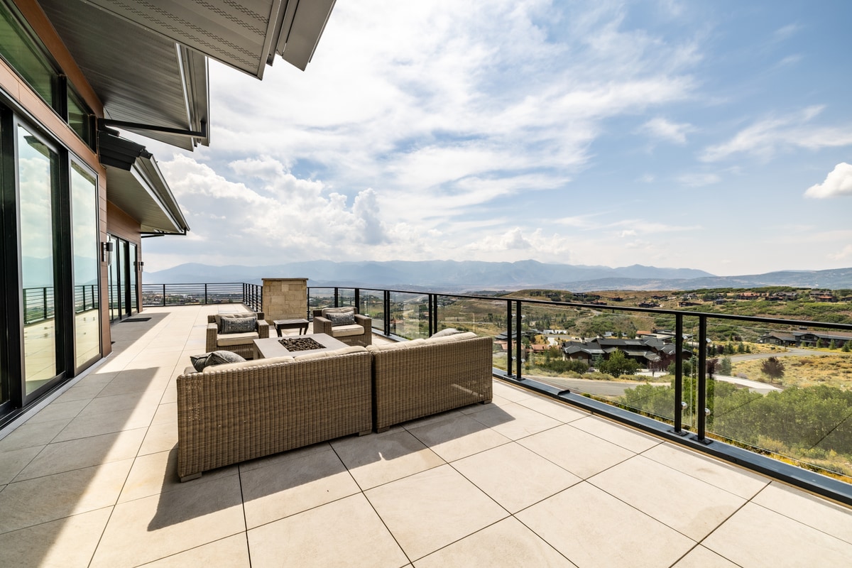 Summit Estates Park City Utah — expansive upper terrace with wicker lounge seating, glass-panel railing, and panoramic valley views